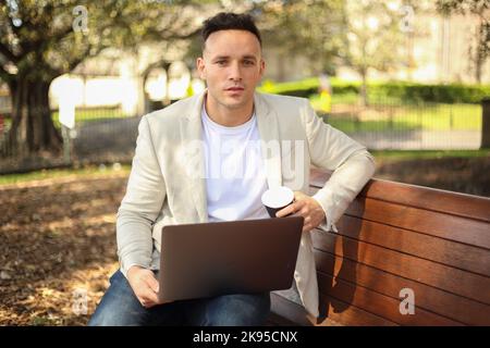 Junger freiberuflicher Mann, der mit seinem Laptop und seiner Kaffeetasse aus der Ferne arbeitet Stockfoto