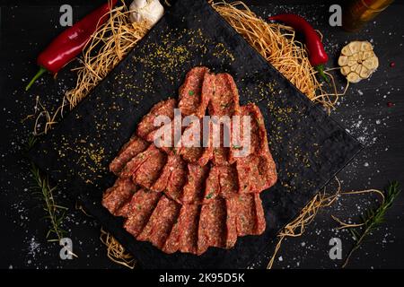 Rohes Hackfleisch auf schwarzem Steinteller. Geformtes Hackfleisch Stockfoto