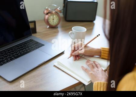 Eine Frau, die mit einem Bleistift Erinnerungen in ein Notizbuch schreibt Stockfoto