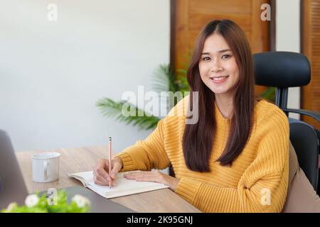 Eine Frau, die mit einem Bleistift Erinnerungen in ein Notizbuch schreibt Stockfoto