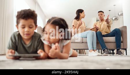 Mutter, Vater und Uneinigkeit über das Sofa im Wohnzimmer, während die Kinder zu Hause mit dem Tablet auf dem Boden spielen. Mama und Papa kämpfen, streiten oder Stockfoto