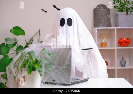 Ghost of Halloween nutzt Laptop im Internet surfen, Online-Shops durchsuchen, Märkte. Ein Geist macht eine Bestellung vom Computer für Halloween. Ghost zahlt für den Online-Kauf per Kreditkarte. Stockfoto