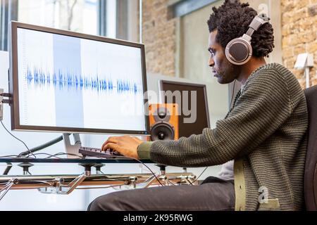 Die Medienagentur: Toningenieur. Ein Musikproduzent bei der Arbeit in seinem Aufnahmestudio - generische Wellenform auf dem Bildschirm. Aus einer Reihe verwandter Bilder. Stockfoto