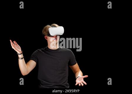 Junger Mann trägt Virtual Reality VR-Brille, Brille isoliert auf schwarzem Hintergrund. In Einer Metaverse Stockfoto