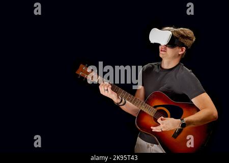 Mann spielt Gitarrenspiel in Virtual Reality Helm. VR-Brille, Brille, auf schwarzem isolierten Hintergrund Stockfoto