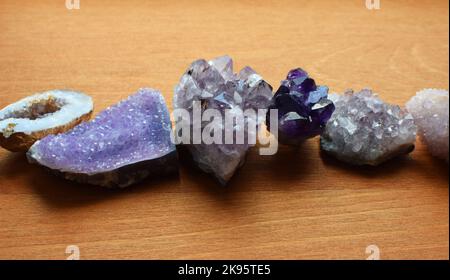 Wunderschöne violette Kristalle und Amethyst drusen liegen auf einem hölzernen Hintergrund. Magische Amulette. Stockfoto