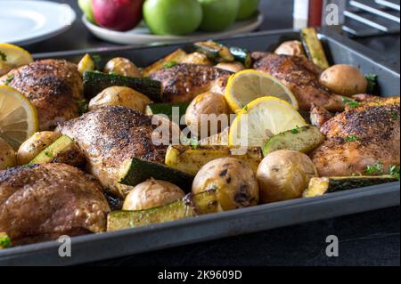 Im Ofen gebackene Hähnchenschenkel mit Kartoffeln und Zucchini auf einem Backblech Stockfoto