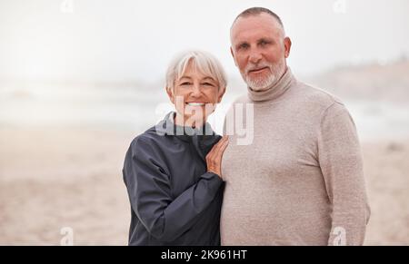 Porträt eines glücklichen und älteren Paares Genießen Sie an einem nebligen Tag ein romantisches Date am Strand. Liebe, Glück und ältere Rentner Mann umarmt Frau Stockfoto