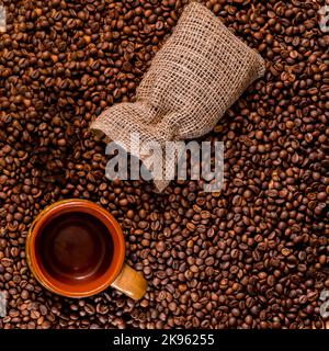 Viele Kaffeebohnen sind auf dem Tisch neben dem Kaffeesack verstreut. Stockfoto