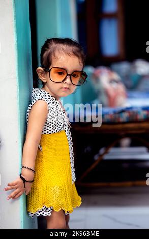 Die vertikale Ansicht eines indischen Mädchens, das an der Wand steht, während es modische Sonnenbrillen trägt Stockfoto