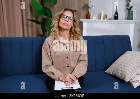 Portrait einer hübschen Psychologin im mittleren Alter mit Clipboard auf dem Sofa im Innenbereich Stockfoto