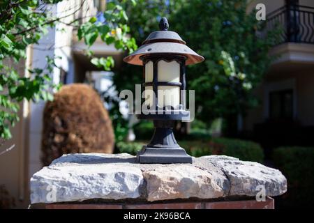 Alte alte alte Straßenlaterne auf einem Ziegelzaun im Garten. Metallic-Laterne im Retro-Stil. Straßenbeleuchtung. Stockfoto