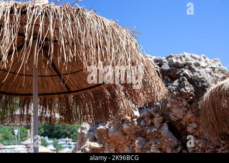 Strohschirm oder Strohhütte mit wunderschönem Blick auf den tropischen Strand. Strohschirme am Strand gegen klaren blauen Himmel Stockfoto