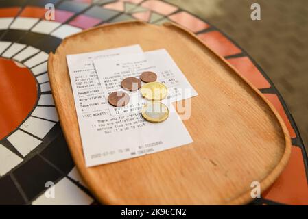 Holztablett in einem Café mit einer Rechnung für die Zahlung und Wechsel in Euro-Münzen. Auf der Straße Stockfoto