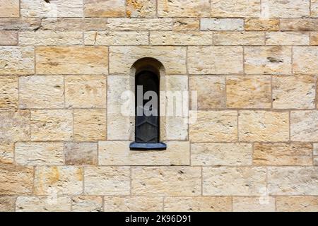 Schmale Fenster, geschlossen mit eisernen Fensterläden, in einer Steinmauer aus roten und beigen Blöcken. Aus der „Window of the World“-Serie. Stockfoto