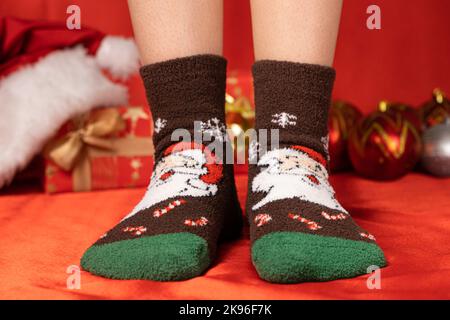 Damenfüße in warmen Weihnachtssocken mit Weihnachtsmann-Nahaufnahme Stockfoto