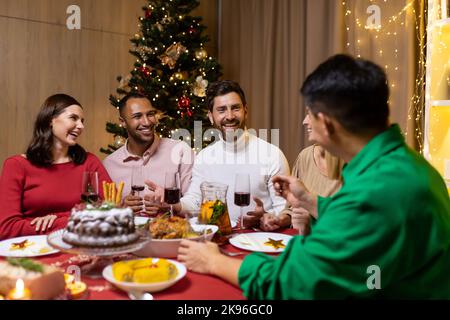 Freunde feiern Weihnachtsabend oder Silvester paty zusammen am Tisch sitzen. Schlemmen Sie zu Hause Gruppe von multi ethnischen festlichen weihnachtsessen. Glückliche fröhliche Menschen klirken Weingläser lachen Stockfoto