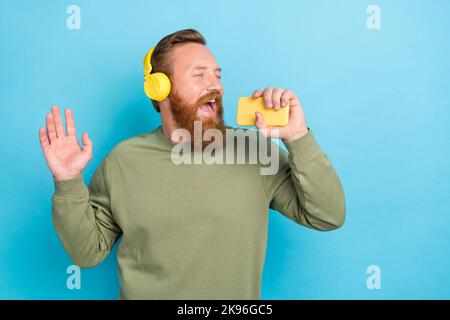 Porträt von sorglosen positiven Kerl mit roten Haaren tragen khaki Pullover singen Lied in Smartphone isoliert auf türkisfarbenem Hintergrund Stockfoto