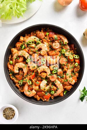 Kreolischer Jambalaya mit geräucherten Würstchen, Hühnerfleisch und Gemüse in einer Pfanne auf weißem Steingrund. Draufsicht, flach liegend Stockfoto