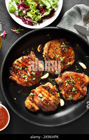 Gebratene Schweinesteaks in einer Pfanne auf schwarzem Stein. Draufsicht, flach liegend, Nahaufnahme Stockfoto