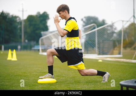 Fußballspieler bei Stretching and Balance Training Unit. Spieler, der auf dem Trainingsfeld ein Balancing-Kissen anlegt Stockfoto