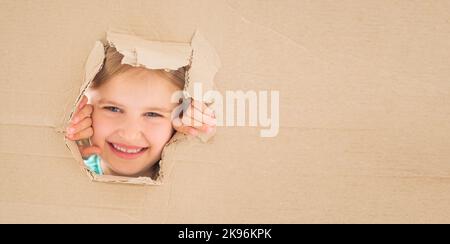 Kleines Mädchen schaut aus dem Loch in Pappe Stockfoto