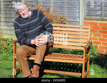 Älterer oder älterer Mann, der an Arthritis im Knie oder Bein leidet. Seine Beine in Qualen haltend. Stockfoto