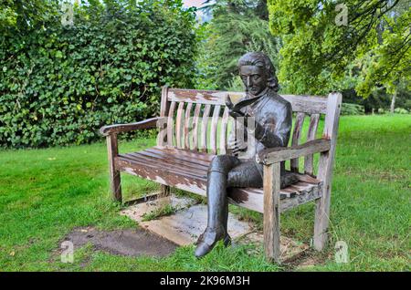 Bronzeskulptur von Gilbert White in seinem Garten, sitzend auf einer Holzbank mit einem Vogel und einem Buch Stockfoto