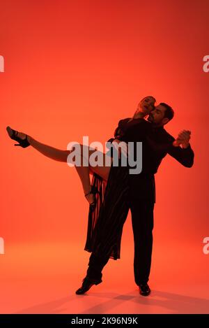 Elegante Frau, die die Hände hält, während sie Tango auf rotem Hintergrund mit Schatten tanzt Stockfoto