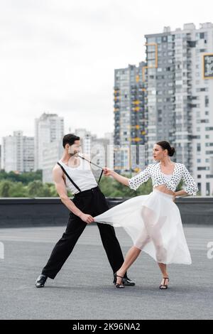 Seitenansicht einer stilvollen Tänzerin in Heels, die mit einem Partner auf dem Dach tanzt Stockfoto