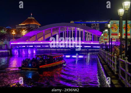 Ein Touristenboot, das den Singapore River entlang fährt und nachts unter der historischen Elgin Bridge vorbeifährt Stockfoto