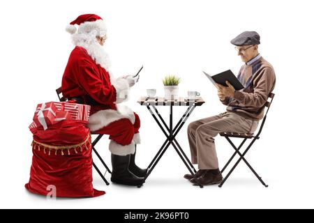 Der Weihnachtsmann mit dem Smartphone und einem älteren Mann, der an einem Tisch sitzt und auf weißem Hintergrund ein Buch liest Stockfoto