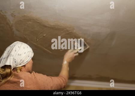 Defokussieren Sie junge Frau bei Hausreparaturen, indem Sie Gips mit einer Kelle auftragen. Frau malt Wand in ihrer neuen Wohnung. Renovierung, Renovierung und Renovierung Stockfoto