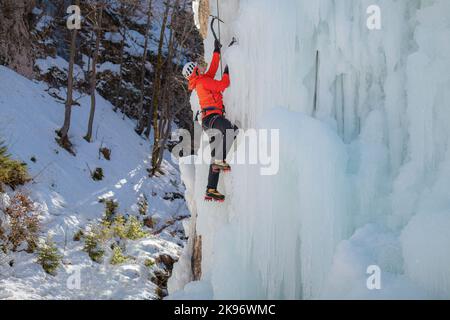 Alpinist Mann mit Eiskletterausrüstung auf einem gefrorenen Wasserfall Stockfoto