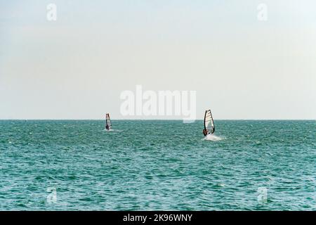Extreme mann Athlet schwimmt auf der Wind Surf auf der sea wave gegen das blaue Meer und den Horizont. Extreme Wassersport. Bewegung der Red Sail auf der Stockfoto