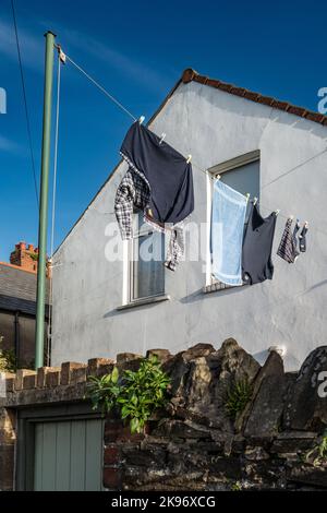 Waschen, das zum Trocknen an einer Wäscheleine vor einem Reihenhaus in Cardiff, Wales, hängt. Bunte Hemden, Haus und Himmel Stockfoto