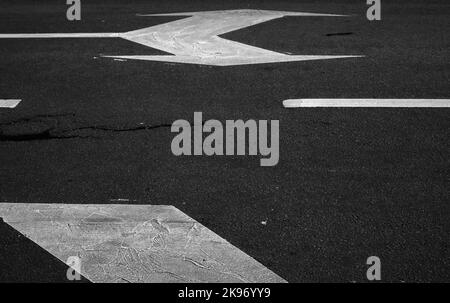 Straßenmarkierung mit weißen Linien und Pfeilen über dunklem Asphalt, abstraktes Transport-Hintergrundbild Stockfoto
