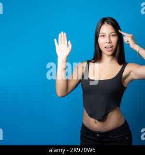 Junge multirassische trendige Frau mit einem großen Lächeln, das den Kopierraum auf der Seite ihrer Handfläche hält und auf blauem Hintergrund isoliert präsentiert Stockfoto