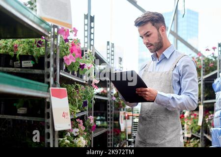 Floristin mit Zwischenablage, die in der Nähe eines Blumenregals steht. Stockfoto