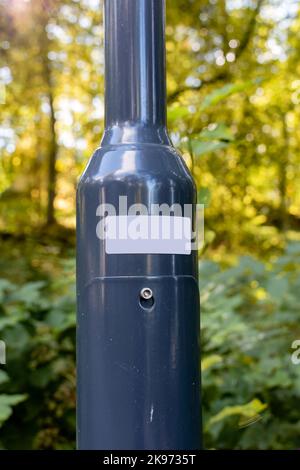 Nahaufnahme eines weißen Sticker auf einem metallischen Lichtpfosten mit Wald im Hintergrund Stockfoto