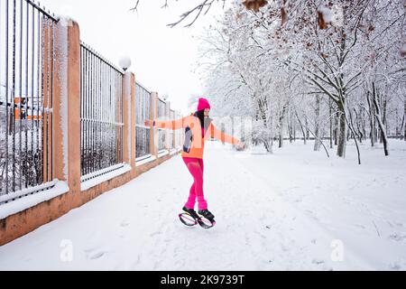 Wintertraining, Training bei kaltem Wetter. Winter Fitness Trening kangoo Sprünge. Sportliche Frau in Sportswear und kangoo-Sprungschuhe springen im Winter Stockfoto