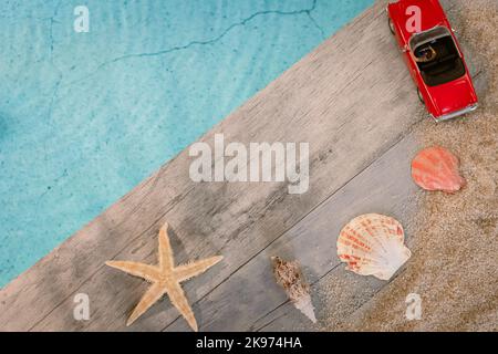 Muscheln von oben auf einem Holzpflaster über einem Pool mit Seesternen gesehen. Atmosphärenurlaub im Sommer. Stockfoto