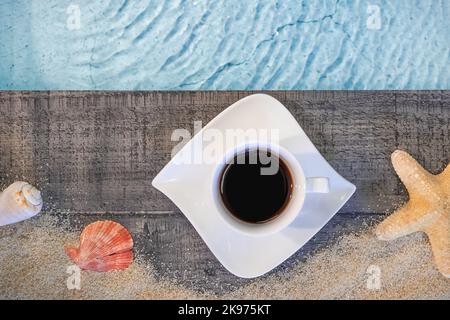 Kaffeetasse von oben auf einem Holzpflaster über einem Pool mit Seesternen. Ambiance Urlaub im Sommer. Stockfoto