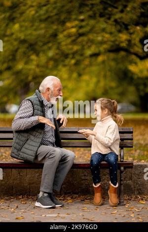 Der gutaussehende Großvater spielt am Herbsttag im Park mit seiner Enkelin ein Spiel mit roten Händen Stockfoto