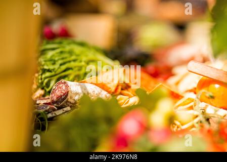 Ein selektiver Fokus einer Salchichon-Wurst auf einem Tisch mit Gemüse, Obst und Kräutern Stockfoto
