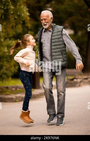 Der gutaussehende Großvater verbringt am Herbsttag Zeit mit seiner Enkelin im Park Stockfoto