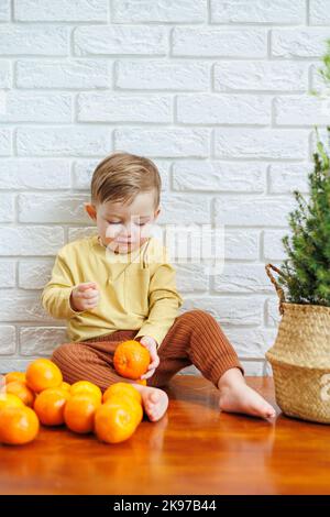 Niedliches lächelndes Kind, das eine frische, saftige Mandarine isst Stockfoto
