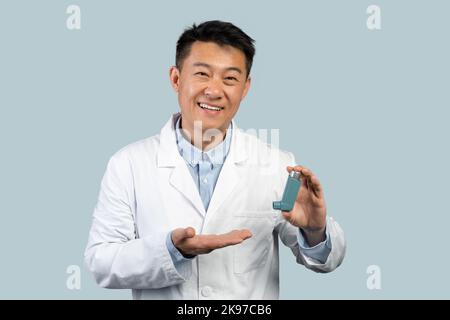 Glücklich mittleren Alters asiatische Mann Arzt in weißem Mantel zeigt Inhalator für die Gesundheitsversorgung Stockfoto