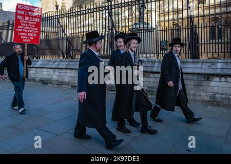 Jüdische Jungs besuchen Westminster in London, dicht gefolgt von einem Mann mit einem Plakat. Stockfoto