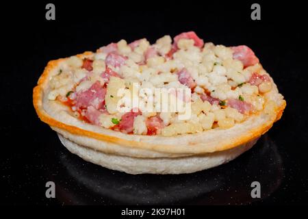 Ungekochte hausgemachte Mini-Pizza auf Tablett auf Tablett im elektrischen Ofen, schwarzer Hintergrund Stockfoto